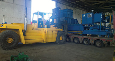 yellow heavy machinery loading blue equipment in warehouse with three containers